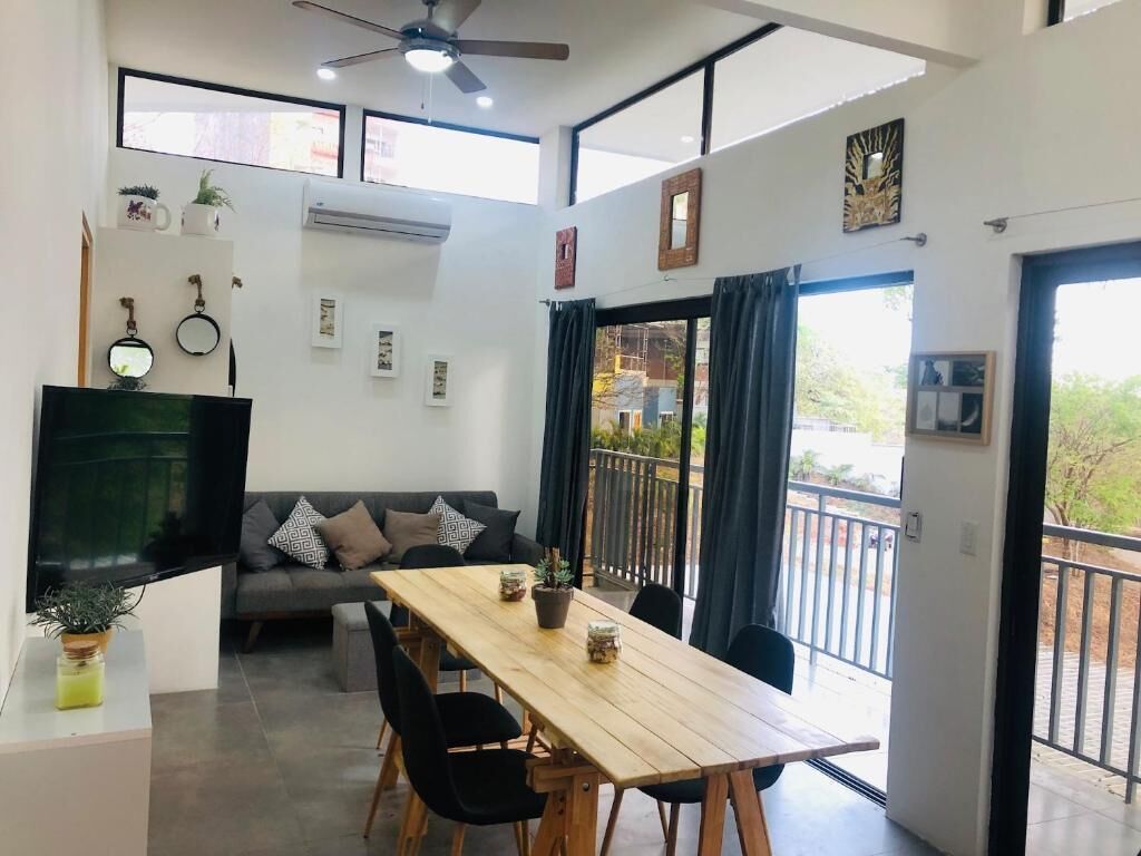 A modern living space with a dining area, a sofa, a TV, and a balcony.