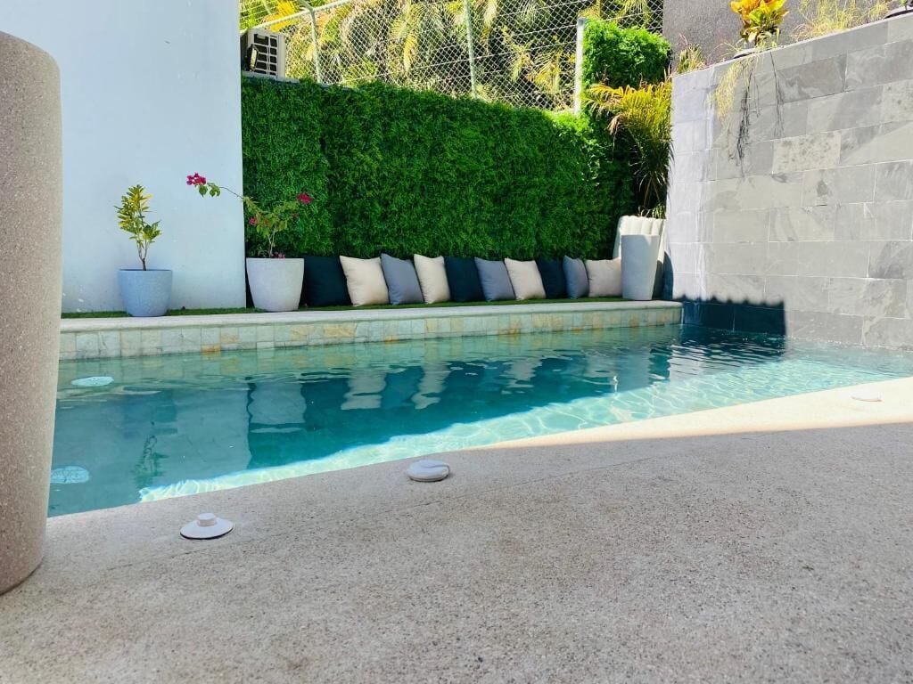 A swimming pool with a stone wall and potted plants.