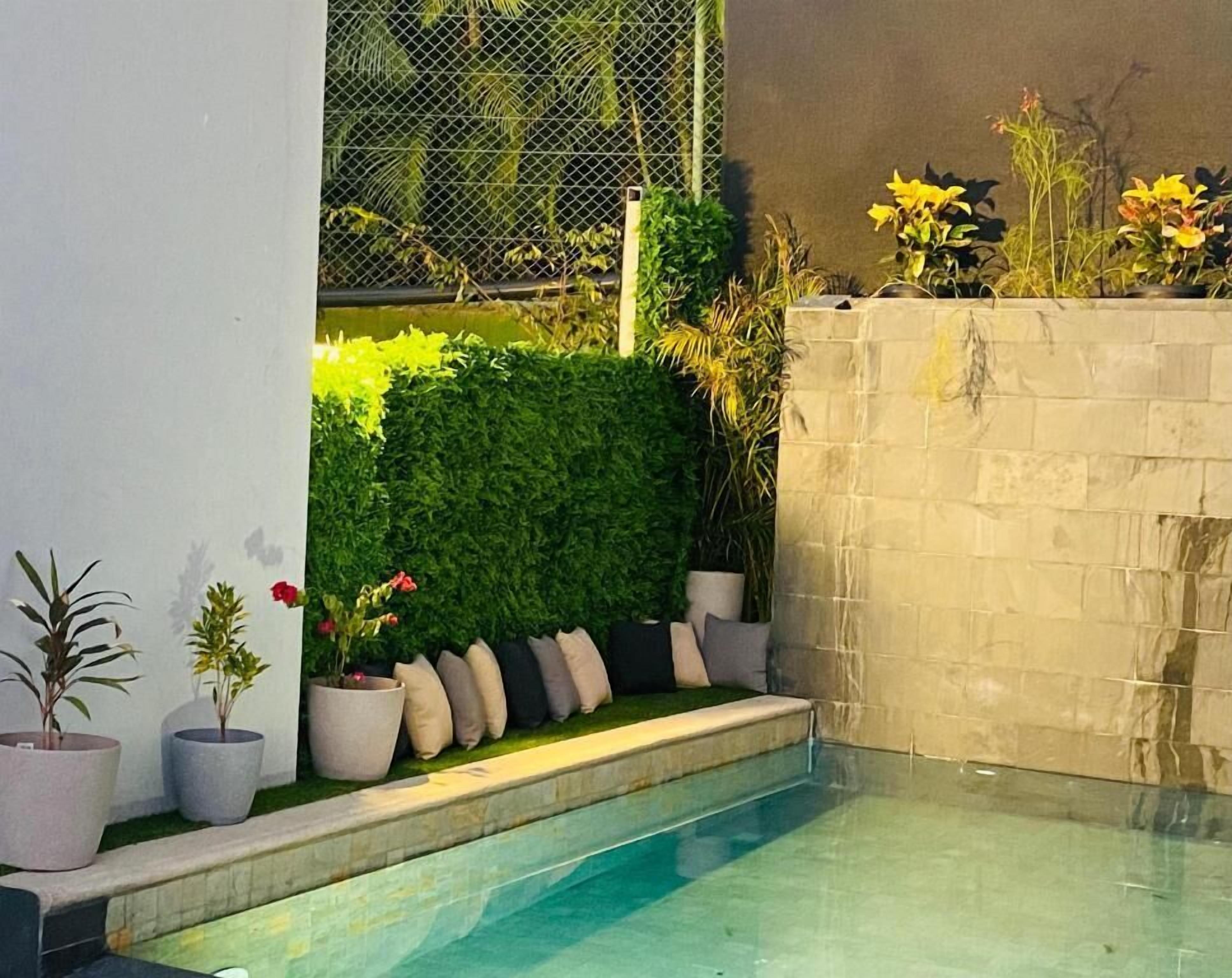 Ein Pool mit Steinmauer, Topfpflanzen und einer Hecke.