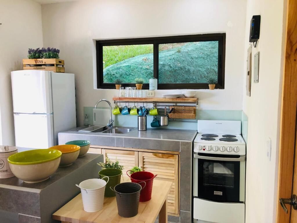 A compact kitchen with a refrigerator, stove, sink, and window with a view of greenery.