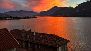 Un atardecer sobre un lago con montañas al fondo y un edificio con techo de tejas en primer plano.