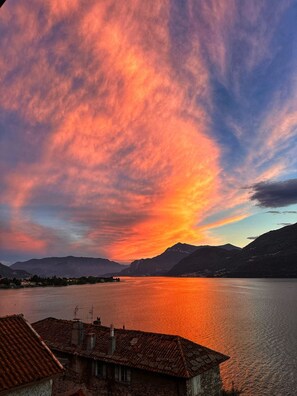 A sunset over a lake with mountains in the background and a building with a tiled roof in the foreground. - Stunning lake view terrace in a medieval village (Dervio)