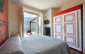 A bedroom with a bed, a TV, a wardrobe, and a balcony with a view.