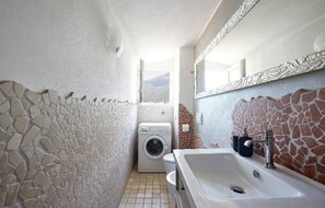 A narrow bathroom with a washing machine, a sink, and a mirror.