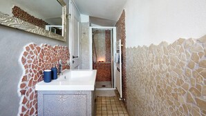 Un baño con un lavamanos blanco, dos botellas azules, un espejo y una zona de ducha con suelo de azulejos.