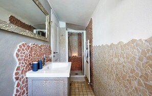 A bathroom with a white sink, two blue bottles, a mirror, and a shower area with a tiled floor.