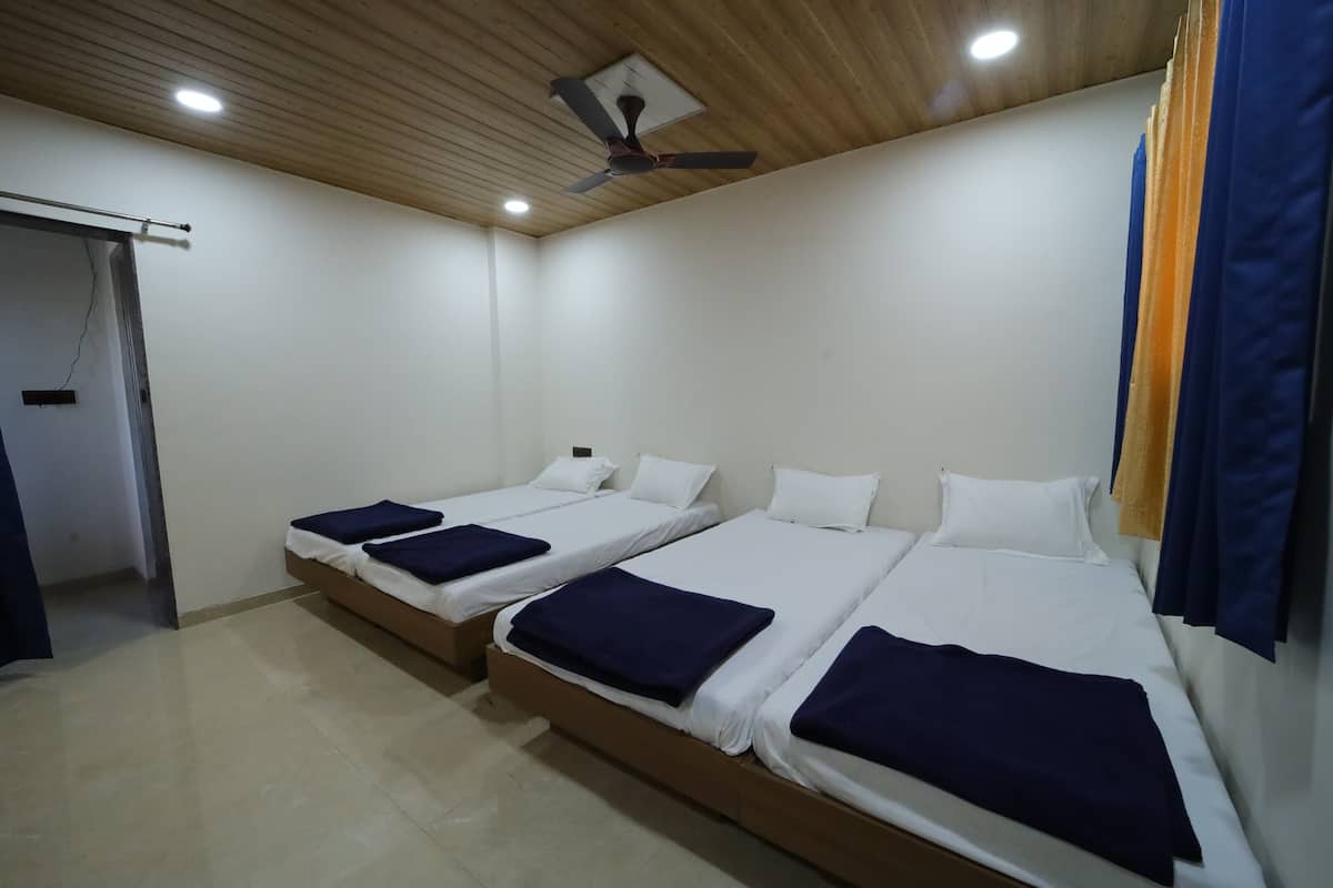 Una habitación con tres camas individuales, suelo de madera, un ventilador de techo y una puerta que da a otra estancia.