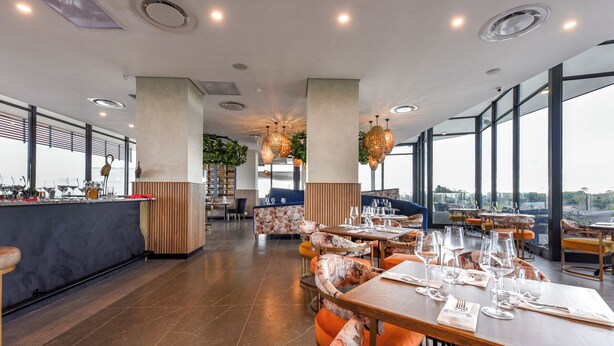 A modern restaurant with high ceilings, large windows, and a mix of seating arrangements including tables and booths.