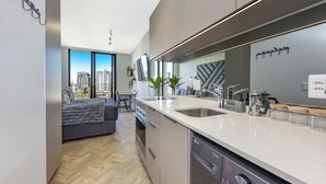 A modern kitchen with a dishwasher, double sink, and a view of the city through large windows.