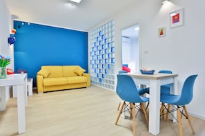 Ein modernes Wohnzimmer mit einem gelben Sofa, einem Esstisch mit blauen Stühlen und einer blauen Akzentwand.