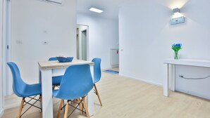 A modern, well-lit room with a dining table, blue chairs, a small side table with a vase, and an air conditioning unit on the wall. - Naples Stay Inn - close to metro & all connections (Napoli)
