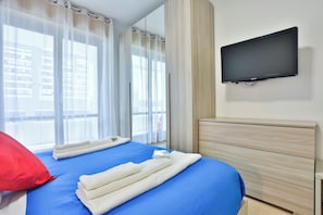Habitación de hotel con una cama, un televisor montado en la pared y una ventana con cortinas.