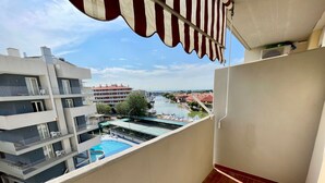 A balcony with a view of a swimming pool, a river, and buildings in the background. - Seaside Apartment With Balcony (Caorle)