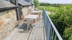Une terrasse en bois avec un muret en pierre, une rambarde en métal et des sièges d’extérieur.