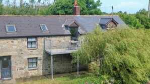 Une maison en pierre avec un balcon, une cheminée et un jardin où poussent des fleurs roses.