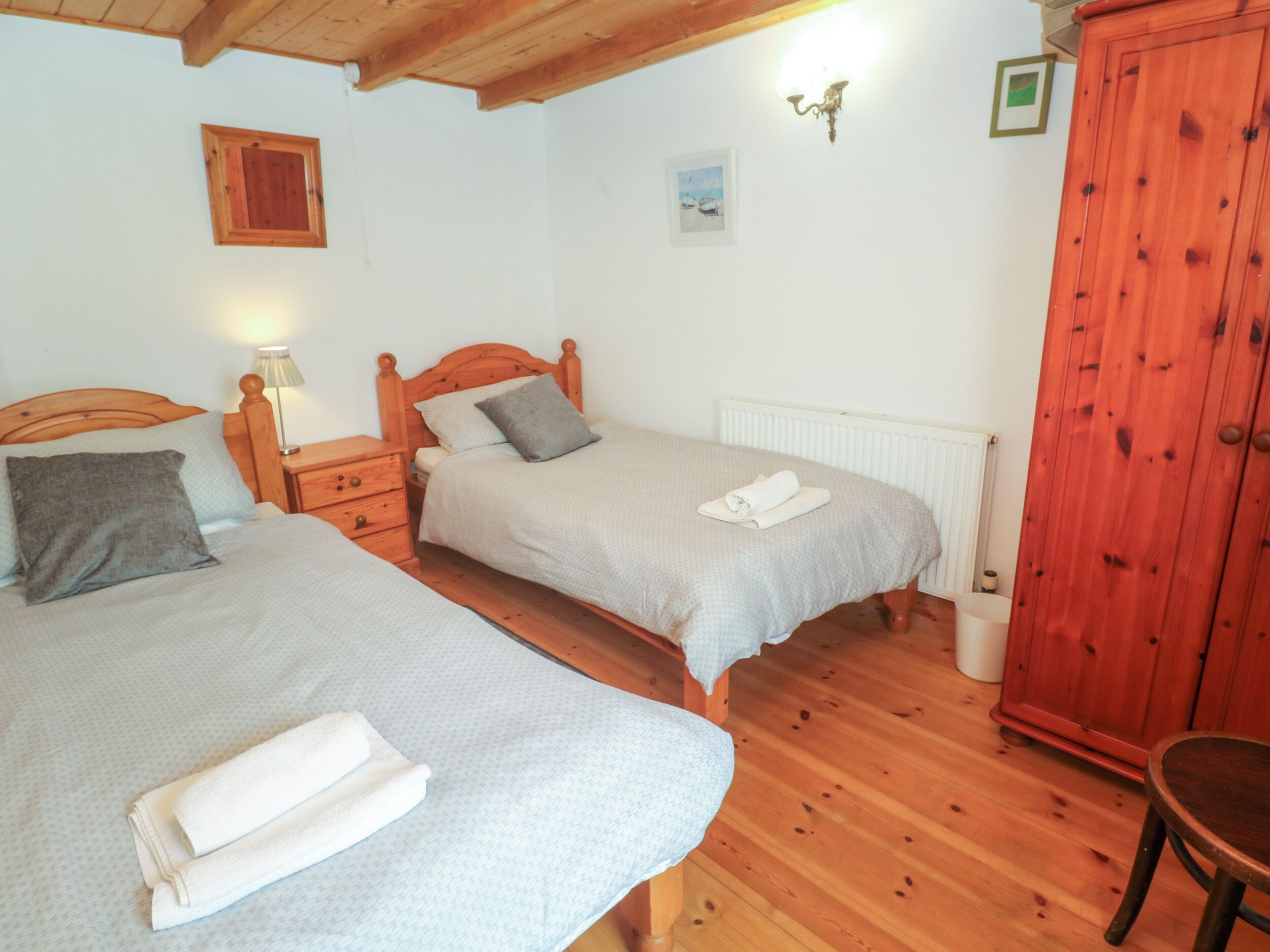 Ein Schlafzimmer mit zwei Betten, Holz-Kopfteilen, einem Holzschrank und einem kleinen Tisch.