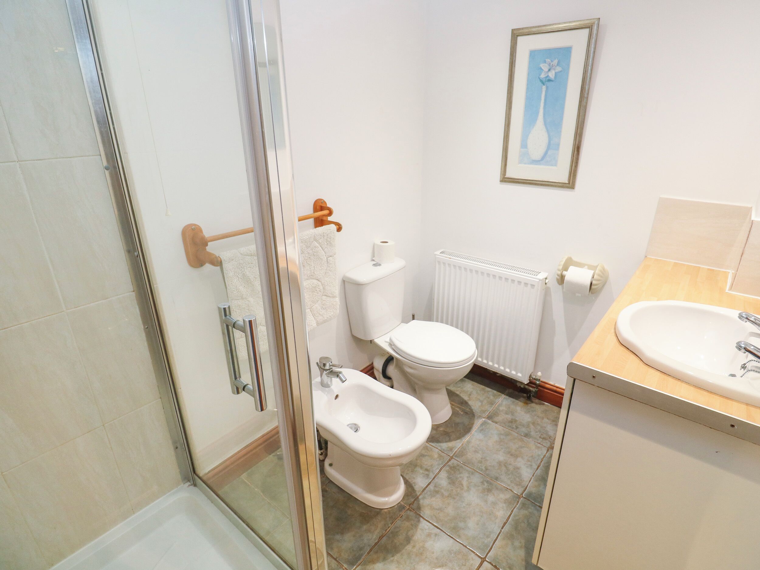 A bathroom with a glass shower enclosure, a toilet, bidet, and a sink.