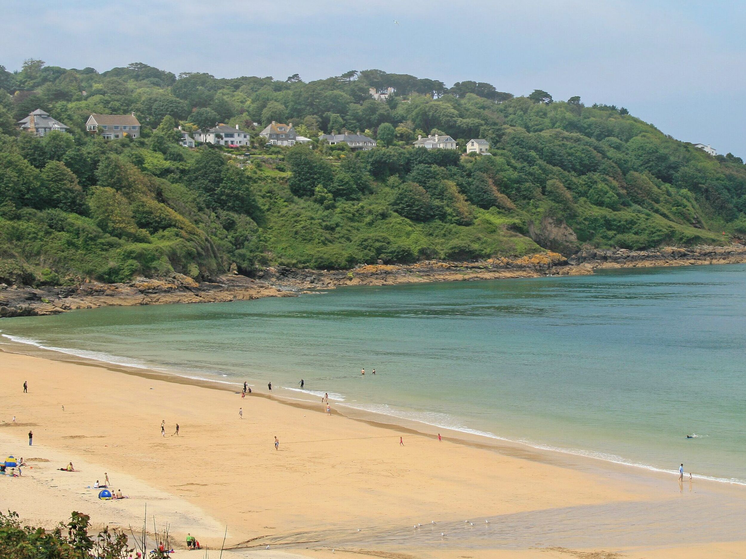 Une plage avec des maisons sur une colline, une eau cristalline et des gens sur le sable.