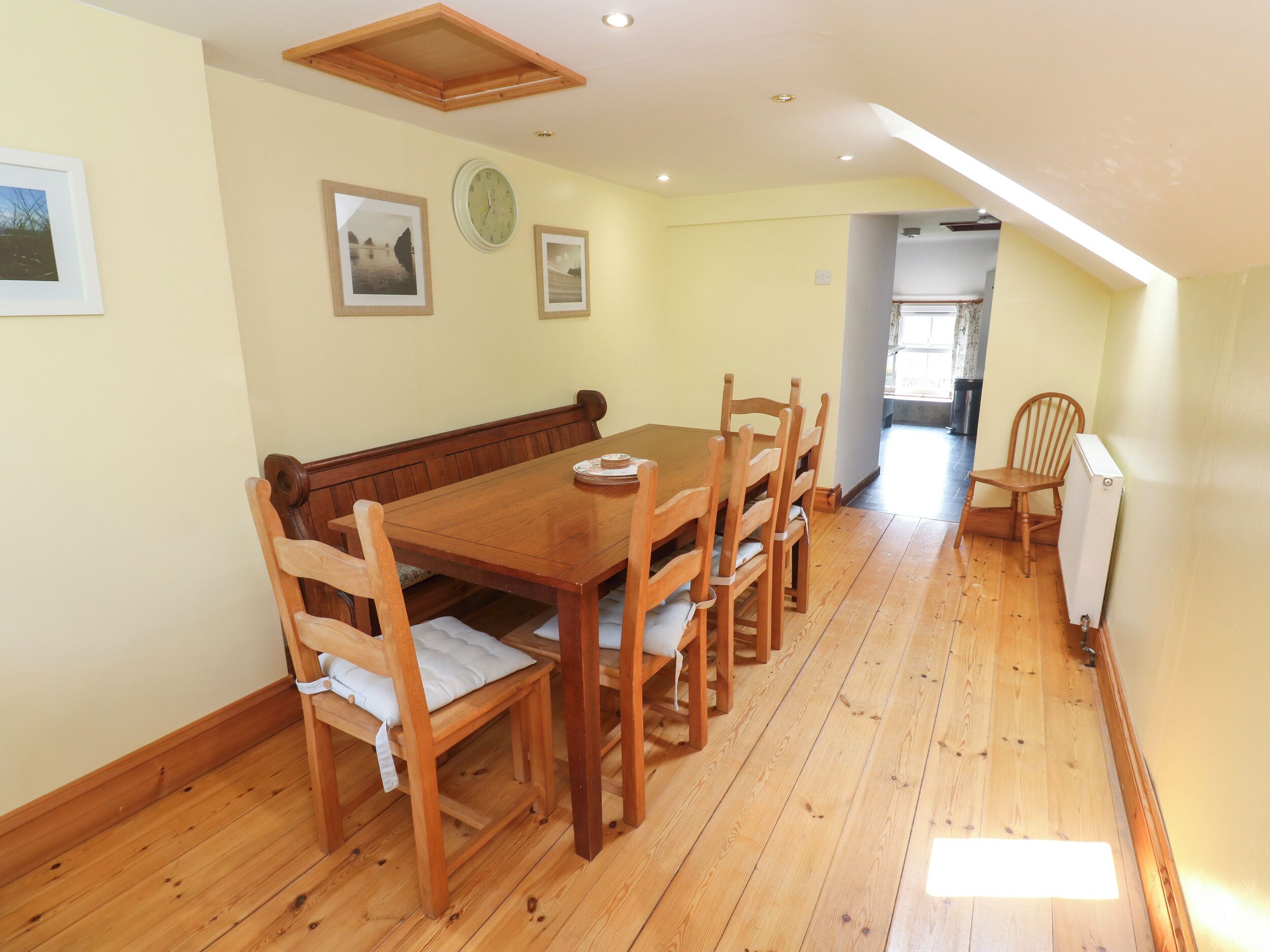 A dining area with a wooden table and chairs, a bench, and framed pictures on the wall.