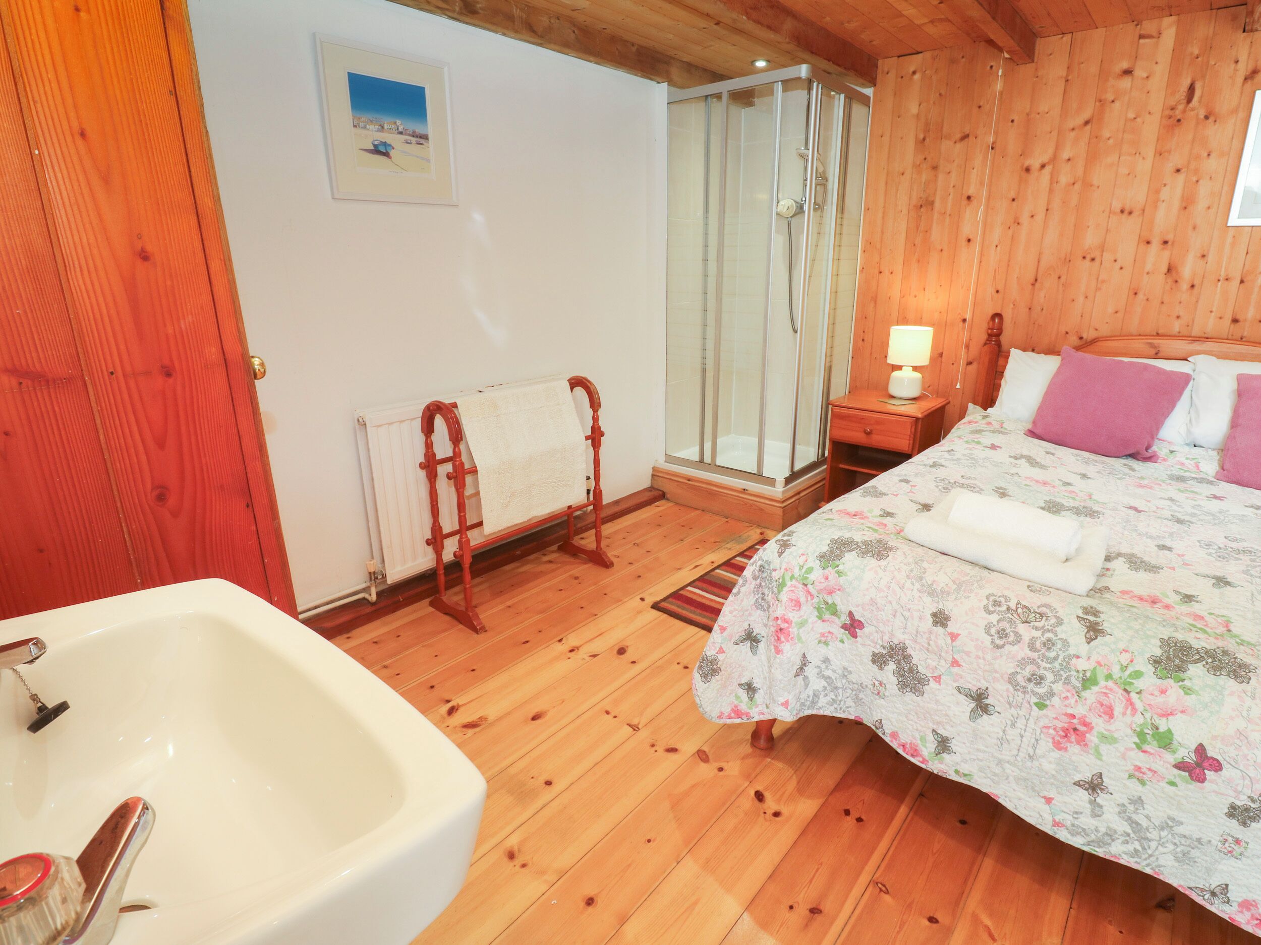 Ein Schlafzimmer mit Holzwänden, einem Bett, einem Nachttisch mit Lampe, einer Duschkabine und einem Heizkörper.