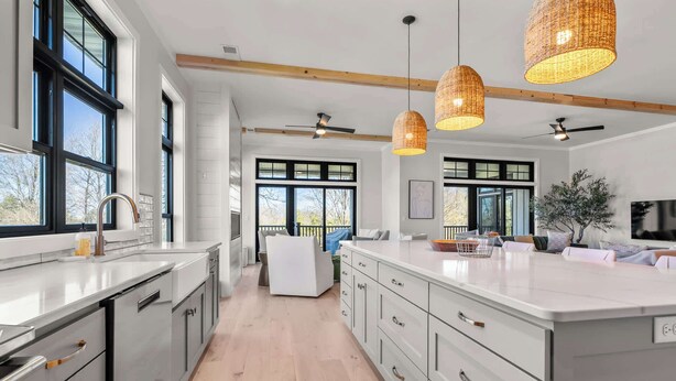 Una cocina moderna con armarios blancos, una isla grande, luces colgantes y vistas al exterior.