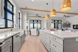 A modern kitchen with white cabinetry, a large island, pendant lights, and a view to the outdoors.
