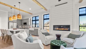 Una sala de estar moderna con chimenea, sofás grises y un comedor con cocina al fondo.
