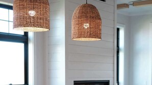 Un comedor moderno con una mesa grande, seis sillas, dos lámparas colgantes de mimbre y una chimenea.
