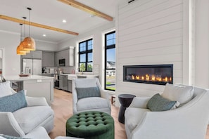 A modern living room with a fireplace, grey sofas, and a kitchen in the background.