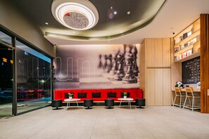 A modern interior with a red seating area, a wall with a large graphic, and a wooden counter with chairs. - Ibis Chengdu Gaoxin Tianfu Software Park Hotel (Chengdu)