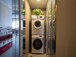 A compact laundry room with stacked washing machines and a glass partition. - Ibis Chengdu Gaoxin Tianfu Software Park Hotel (Chengdu)