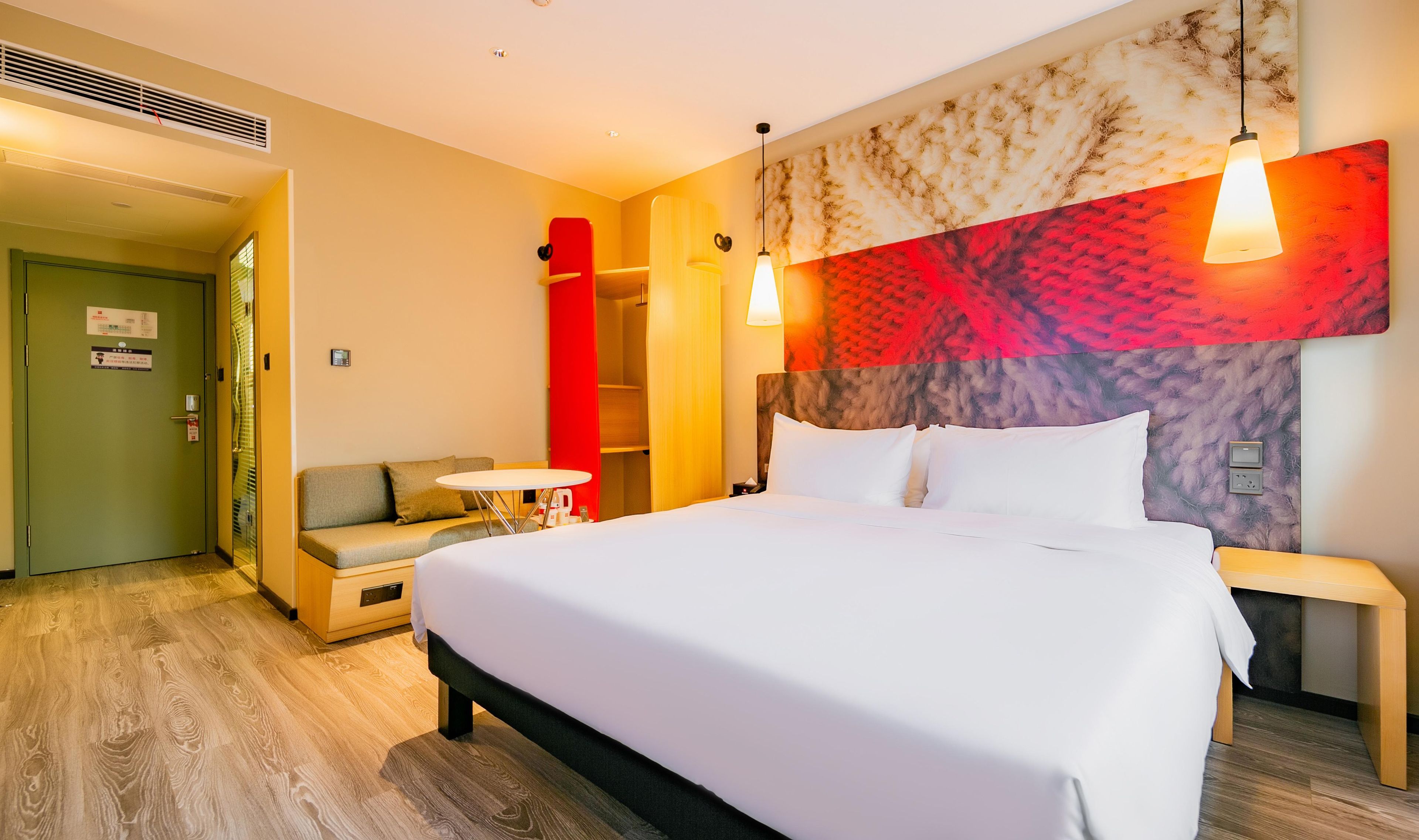 Una habitación de hotel con una cama grande, un sofá, una mesita pequeña y una pared con diseño texturizado.