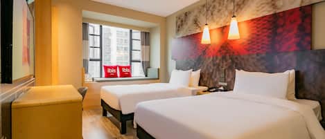 A hotel room with two beds, a wooden desk, a window with curtains, and a wall-mounted artwork.