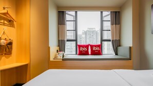A hotel room with a large window, a bed, a bedside table with a lamp, and two red pillows with the hotel name. - Ibis Chengdu Gaoxin Tianfu Software Park Hotel (Chengdu)