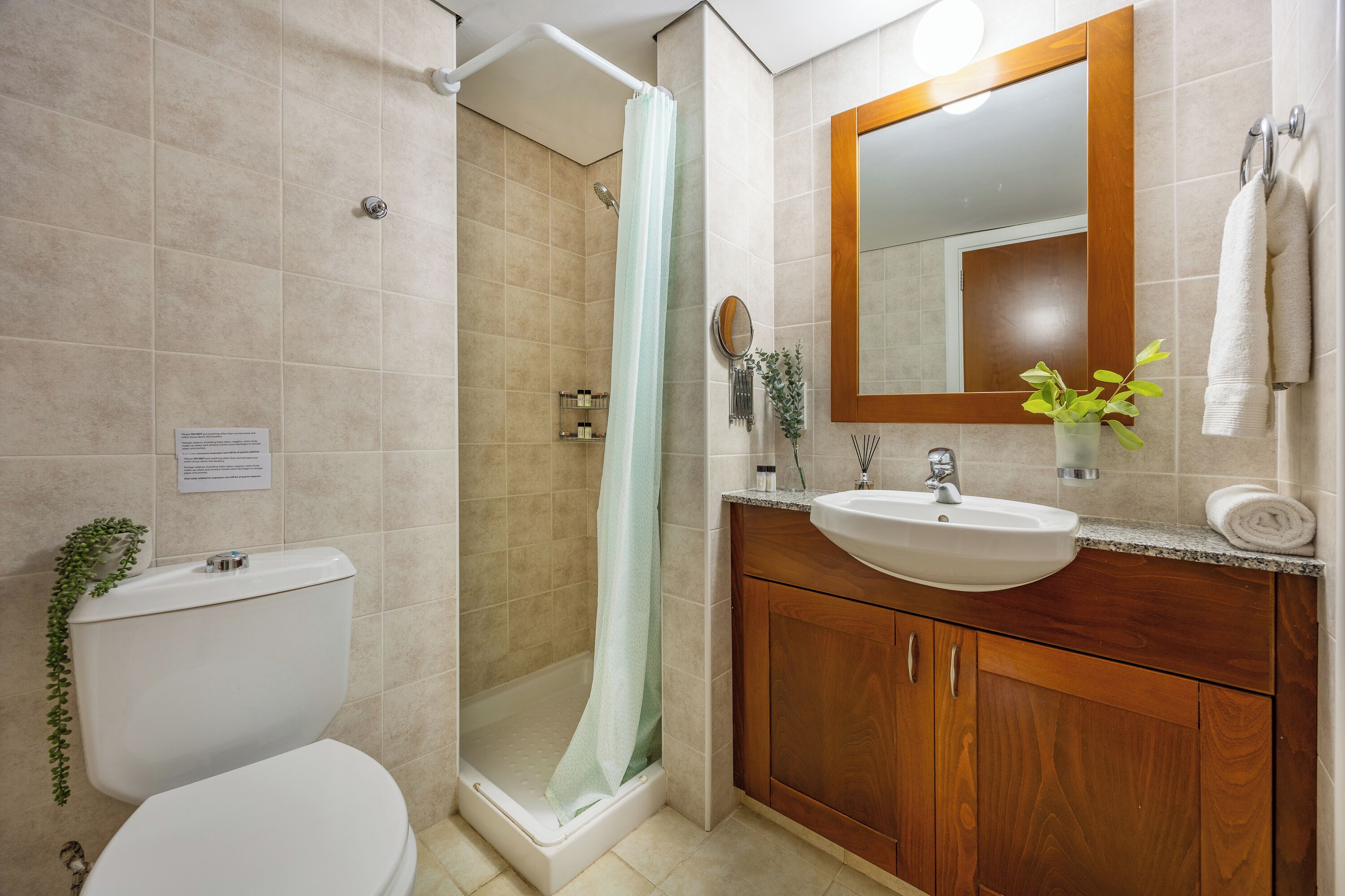 A bathroom with a toilet, shower, sink, and wooden cabinets.