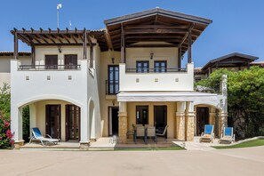 A two-story house with a covered patio, a balcony, and a small outdoor seating area with chairs and a table.
