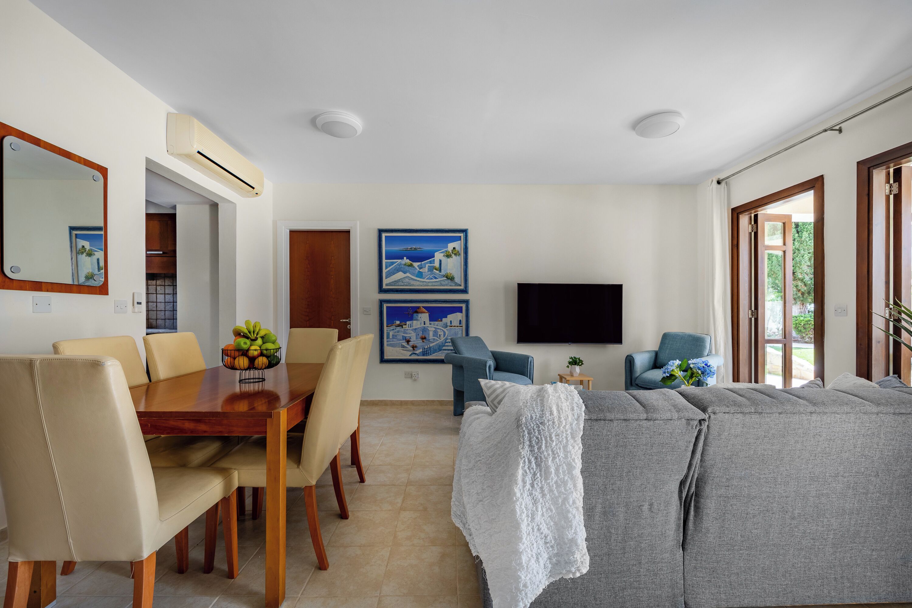 A modern living room with a dining area, a sofa, a TV, and artwork on the walls.