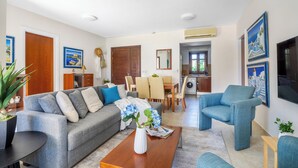 A living room with a sofa, coffee table, and a dining area with chairs and a table. - Da02 Adjacent to Aphrodite Hills Pool View (Kouklia)