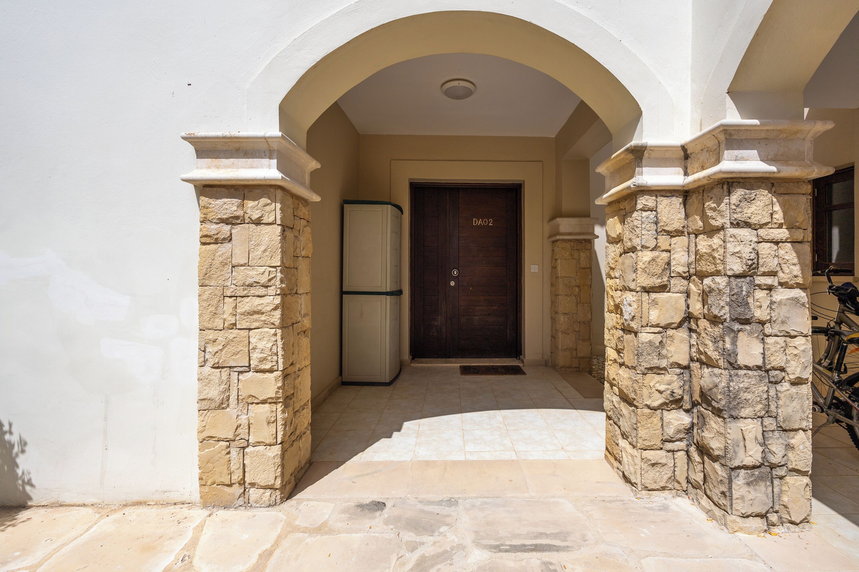 A building entrance with a stone archway, a door labeled "DAO2", and a refrigerator to the left.