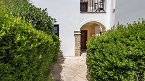A white building with a stone pathway, an arched entrance, and a balcony with a black railing. - Da02 Adjacent to Aphrodite Hills Pool View (Kouklia)