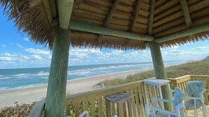 A wooden gazebo with a thatched roof overlooking a beach.