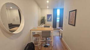 A narrow hallway with a round mirror, a dining table with two chairs, a small plant, and a framed picture on the wall.