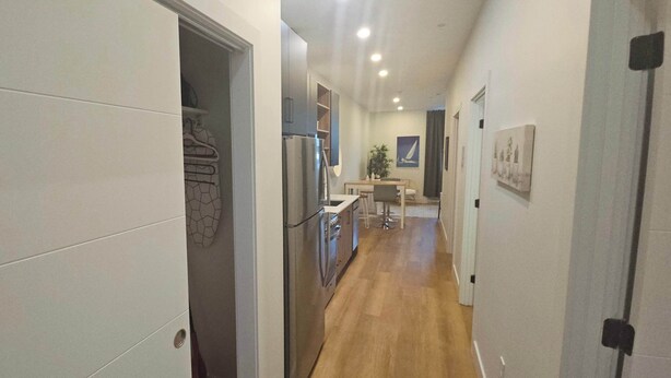 A narrow hallway with a kitchen area at the end, featuring a refrigerator, stove, and dining table.