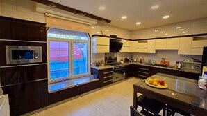 A modern kitchen with dark cabinetry, a built-in microwave, and a large window overlooking a balcony. - Charming 3-bedroom scenic villa with a pool, WiFi in the lovely north (يبلا (إربد))