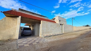 A building with a red-tiled roof, a parked car, and a checkered pavement leading to the entrance. - Charming 3-bedroom scenic villa with a pool, WiFi in the lovely north (يبلا (إربد))