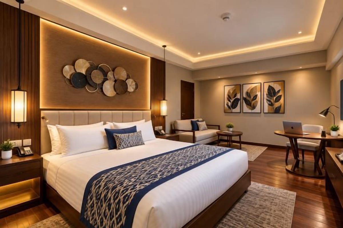 A modern hotel room with a large bed, bedside tables, a desk, and a seating area.
