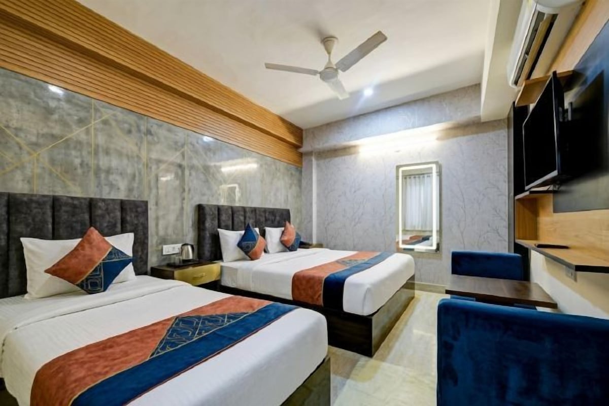 A hotel room with two beds, a desk, a chair, a television, and a ceiling fan.