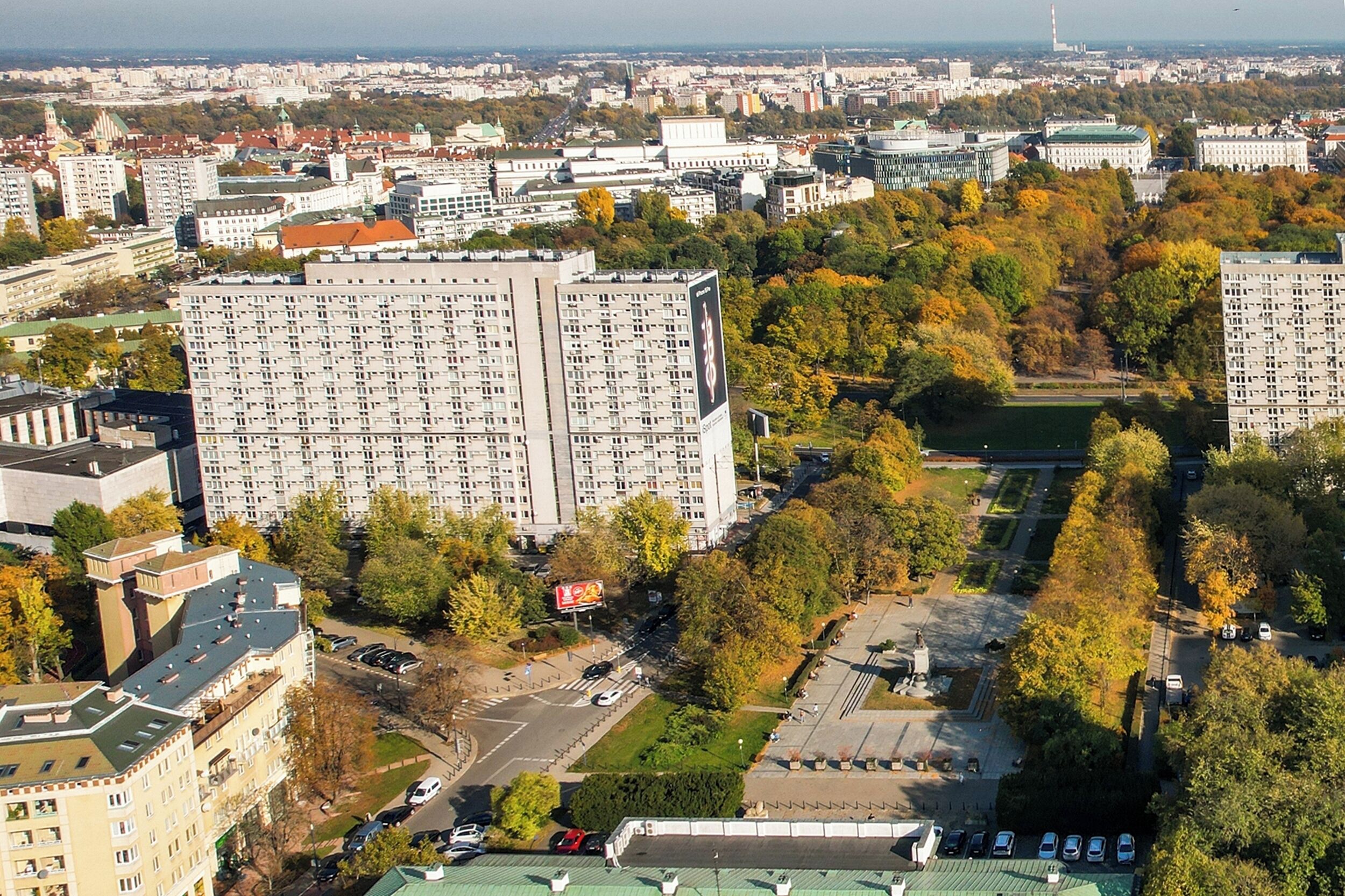 A high-rise building with a grid of windows, surrounded by trees and other buildings.