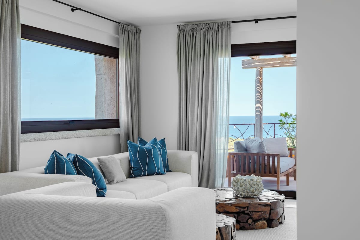 A modern living room with a sectional sofa, a wooden coffee table, and a view of the sea through large windows.