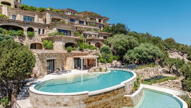 A luxurious villa with a large, curved swimming pool surrounded by stone walls and a stone staircase leading to a covered patio area. - La Tiara di Cervo  (Arzachena)